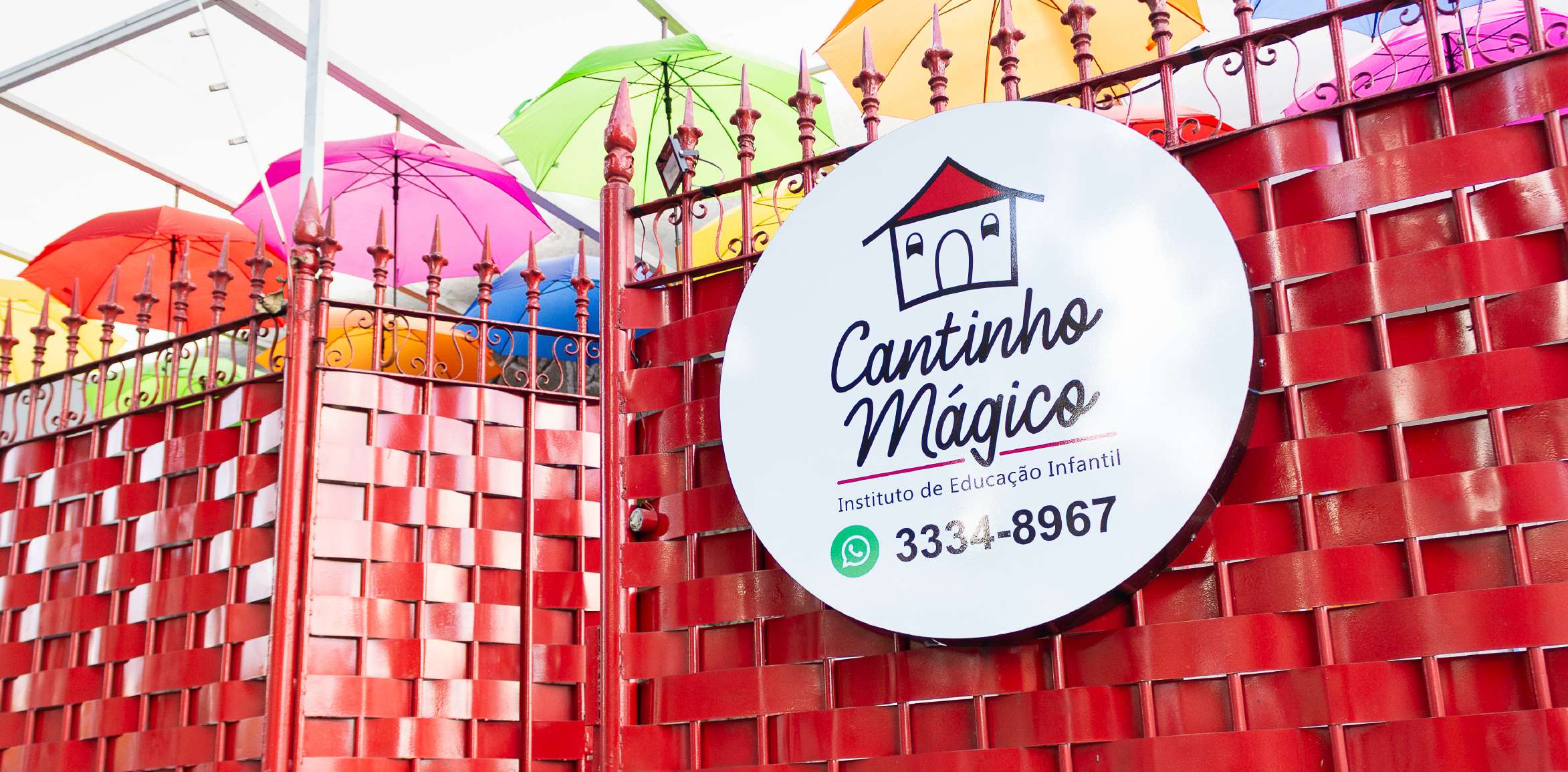 Fachada do Cantinho Mágico com guarda-chuvas coloridos e placa da escola