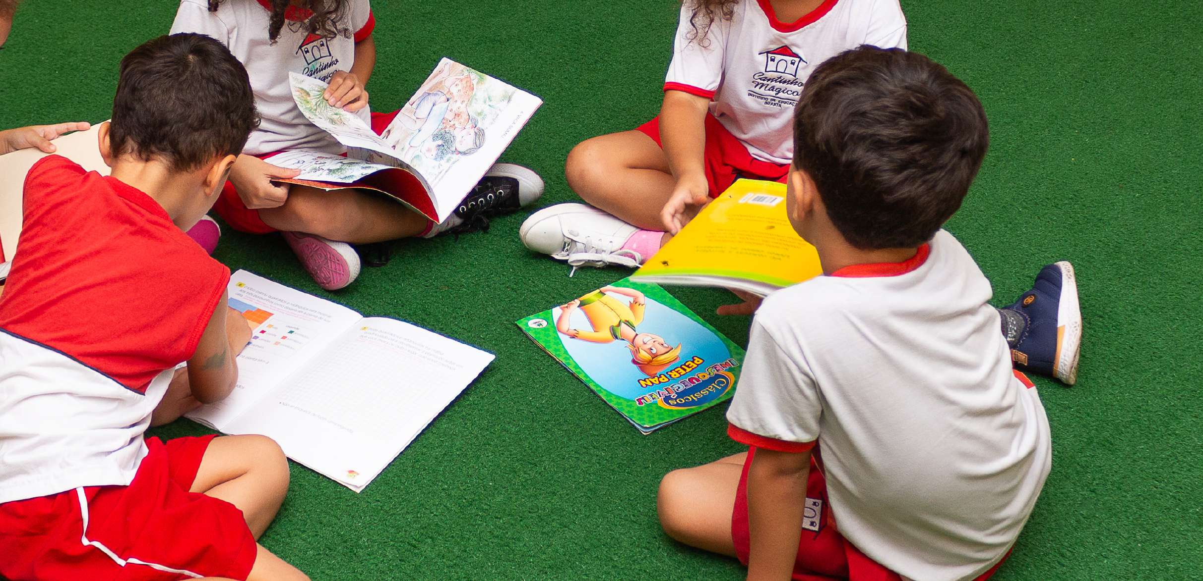 Crianças do Cantinho Mágico lendo livros no gramado da escola